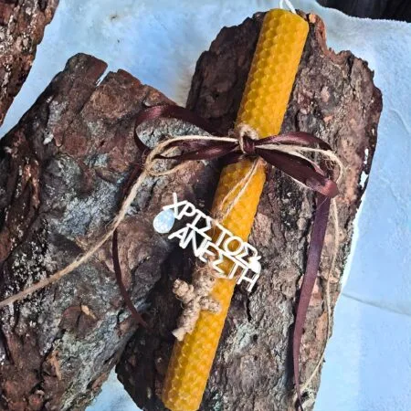 Håndlavet påskelys lavet af naturlig bikage med brunt bånd, naturlig snor, strikket kors, blå perler og indskriften "Kristus er opstanden" på en rustik træbaggrund