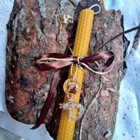 Håndlavet påskelys lavet af bikage med et billede af opstandelsen, bordeauxrødt bånd og et kors lavet af snor på en træstamme