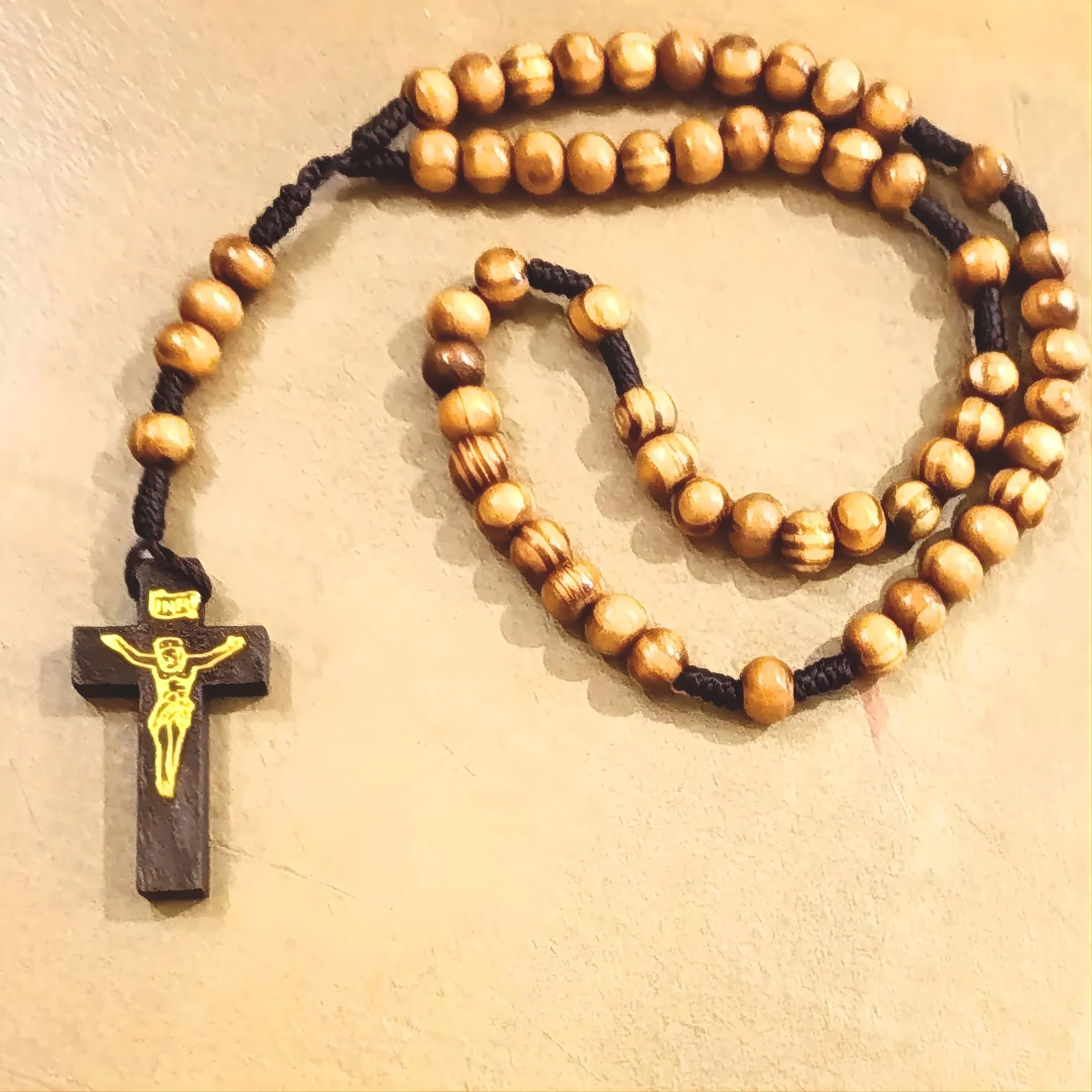 Fotografía cenital de todo el rosario con cuentas de madera de olivo y una cruz sobre un fondo beige.