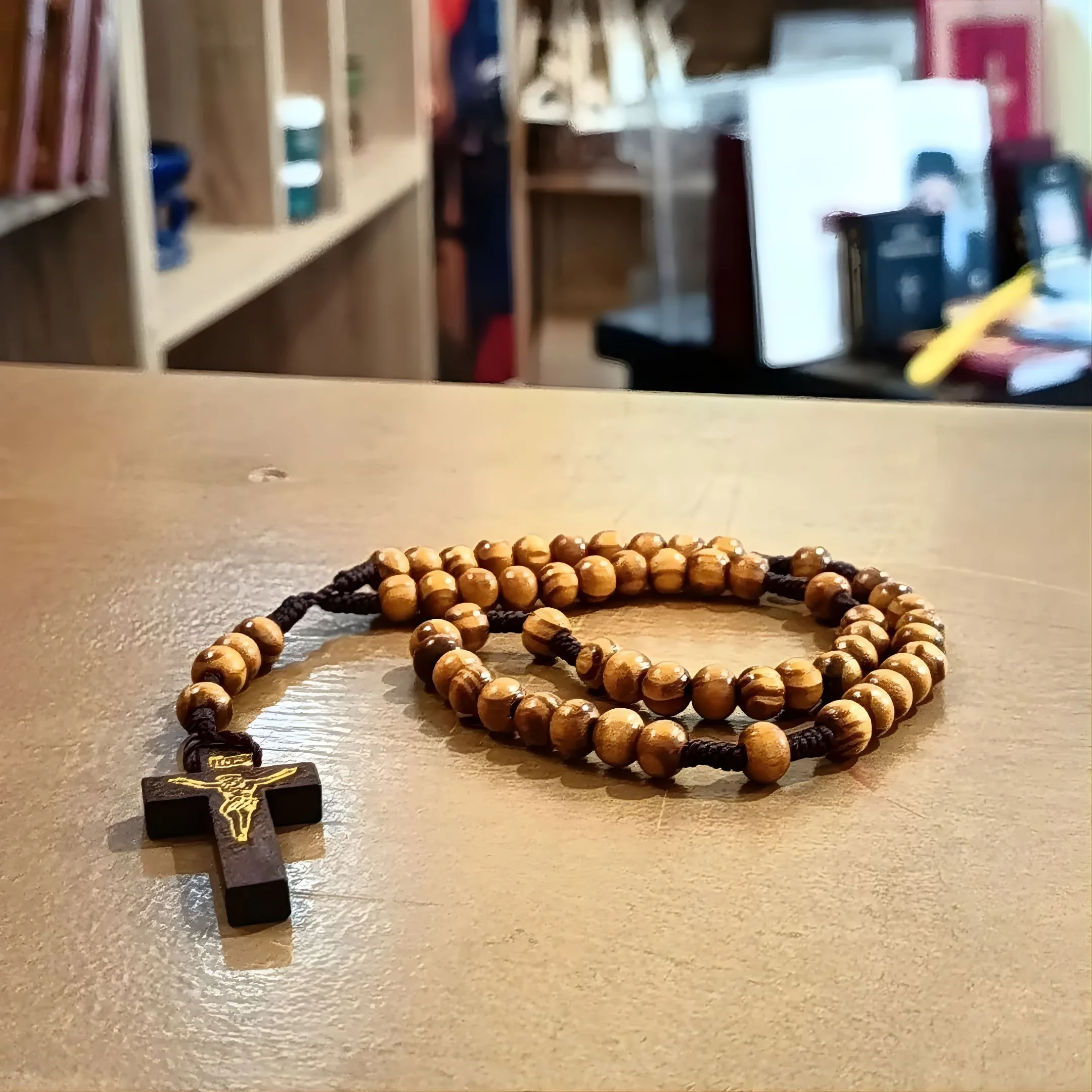 Rosario artesanal con cuentas de madera de color oliva y una cruz de madera con un crucifijo dorado, colocado sobre una superficie de madera.